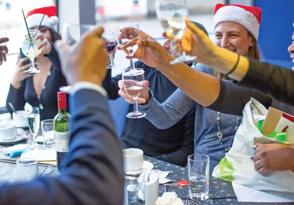 A festive Christmas Party Cruise boat sailing on the Thames during the day with London landmarks, featuring a beautifully set dinner table, live entertainment, and cheerful guests.
